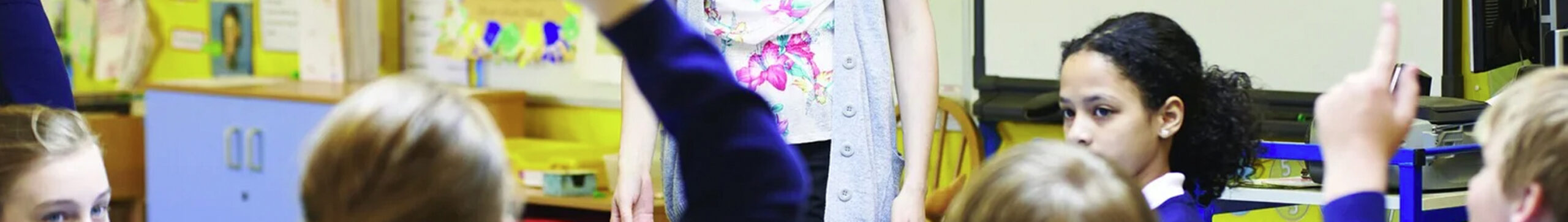 Classroom with child raising hand, teacher at front